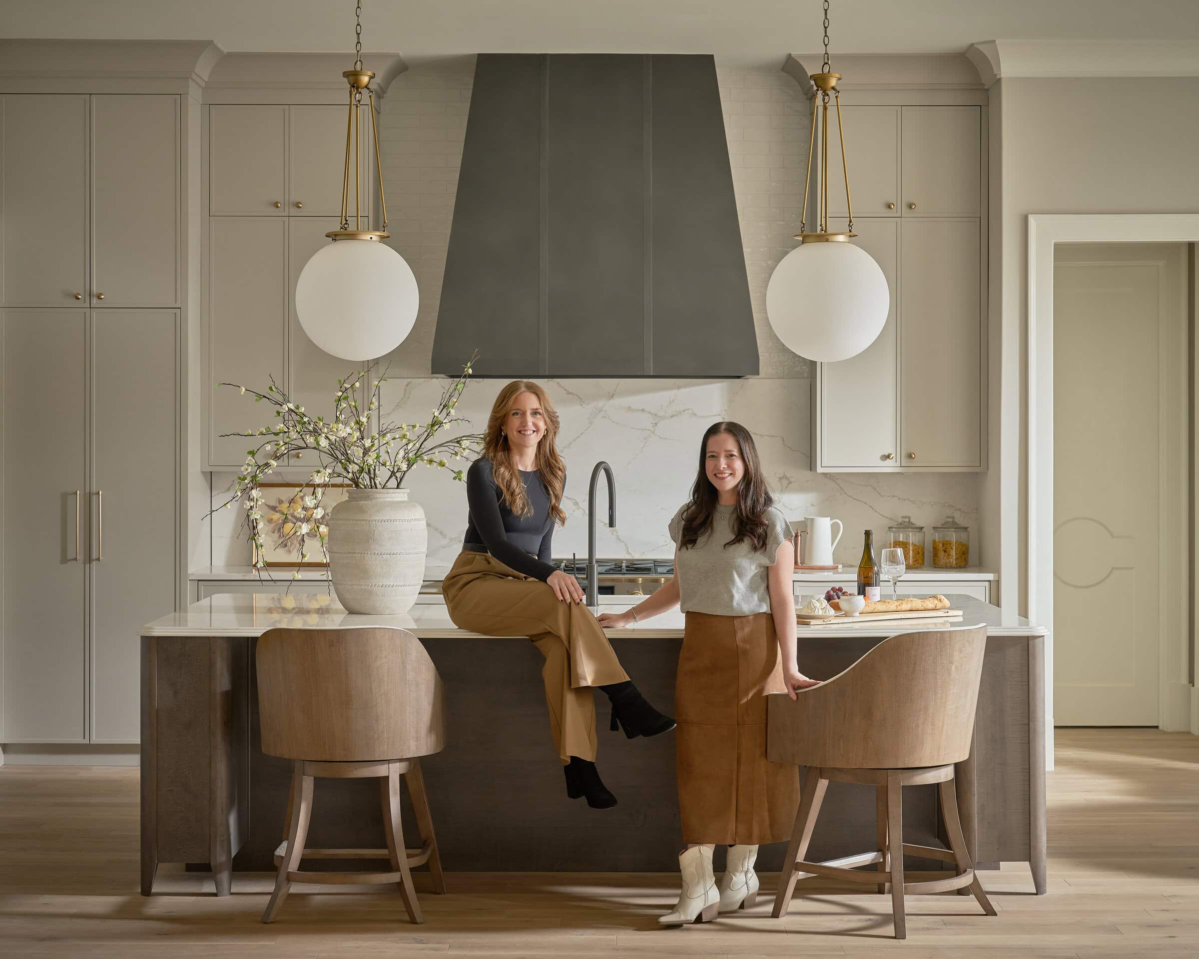 Modern kitchen with two women sitting at the island, featuring sleek cabinetry, pendant lighting, an.